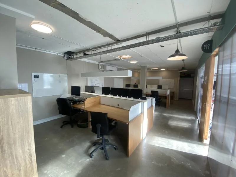 Open-plan coworking office at Lyall Bay Work Hub in Wellington with shared desks, privacy partitions, ergonomic chairs, whiteboard wall, skylights, and natural light throughout the workspace.