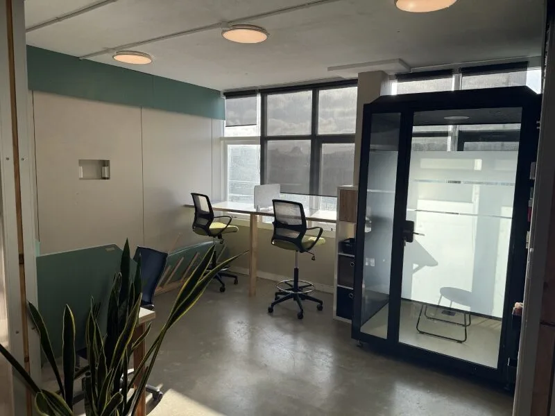 Private office space at Lyall Bay Work Hub in Wellington with window-facing desks, ergonomic chairs, indoor plants, and soundproof phone booth for focused work and video calls.
