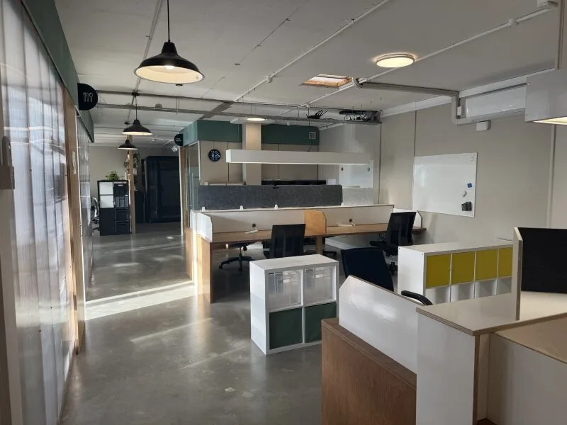 Modern shared coworking space at Lyall Bay Work Hub in Wellington featuring open-plan desks, ergonomic office chairs, natural light, meeting whiteboard, and flexible workspace layout.